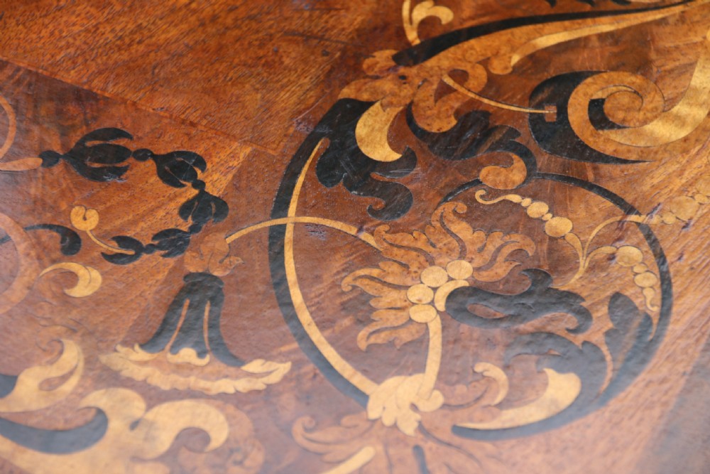 An early 19th-century flame mahogany library table featuring floral marquetry top borders, two frieze drawers with brass knobs, and carved trestle legs connected by a turned stretcher. View XXIX