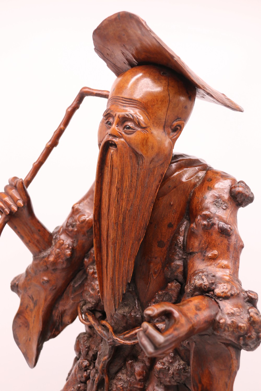 A late 19th-century Chinese carved burr root wood figure depicting a bearded scholar holding a staff, set upon a carved wood base. View XIV