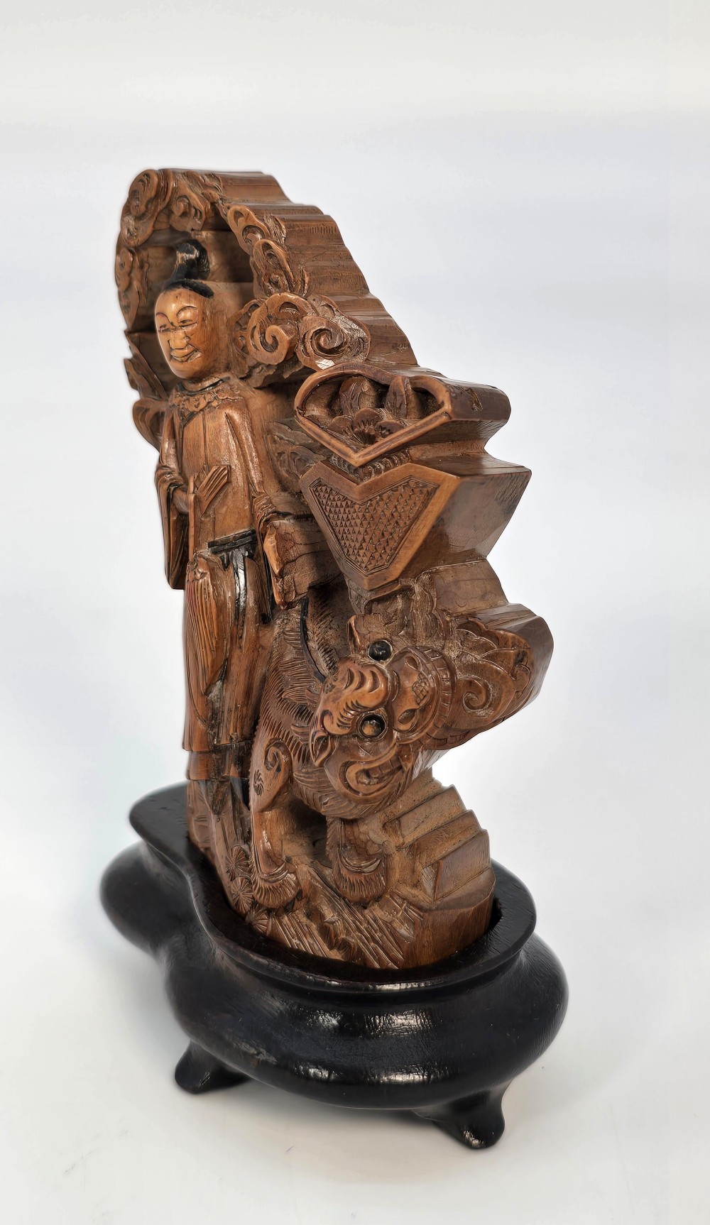 A Japanese carved bamboo okimono figure depicted beside a mythological beast on a dark carved hardwood base.