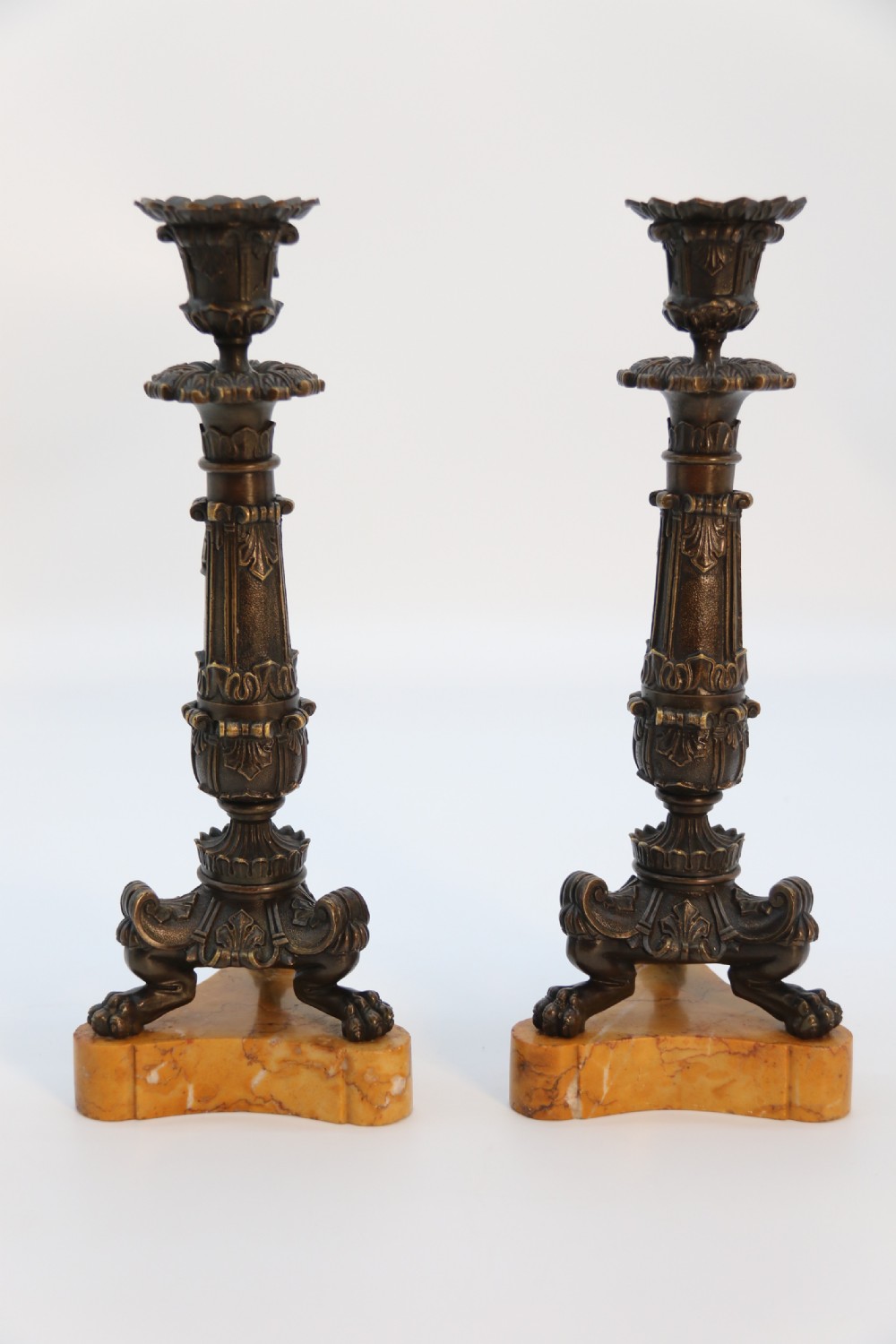 A pair of antique French Empire dark bronze candlesticks with ornate floral carvings and claw feet, resting upon yellow sienna marble plinths. View III