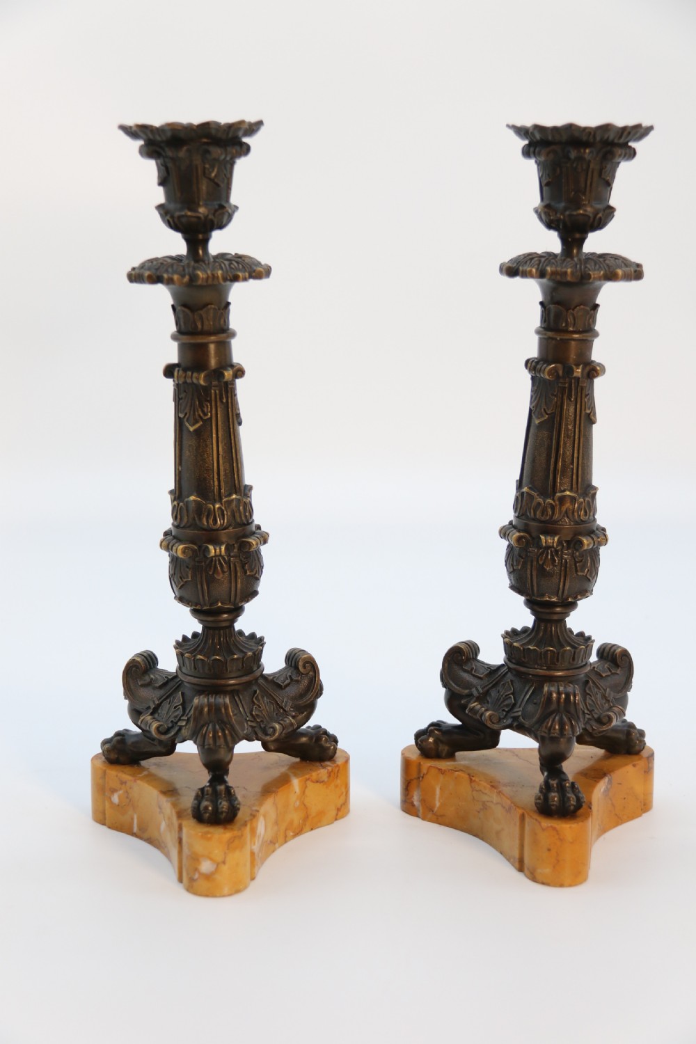 A pair of antique French Empire dark bronze candlesticks with ornate floral carvings and claw feet, resting upon yellow sienna marble plinths. View V