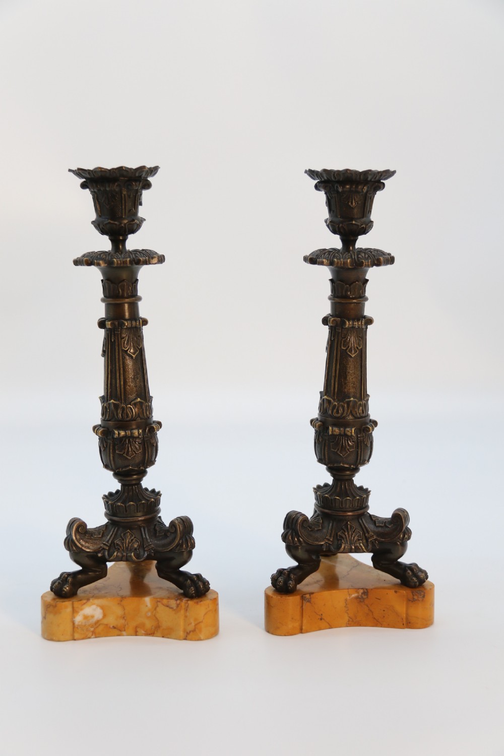 A pair of antique French Empire dark bronze candlesticks with ornate floral carvings and claw feet, resting upon yellow sienna marble plinths. View VI