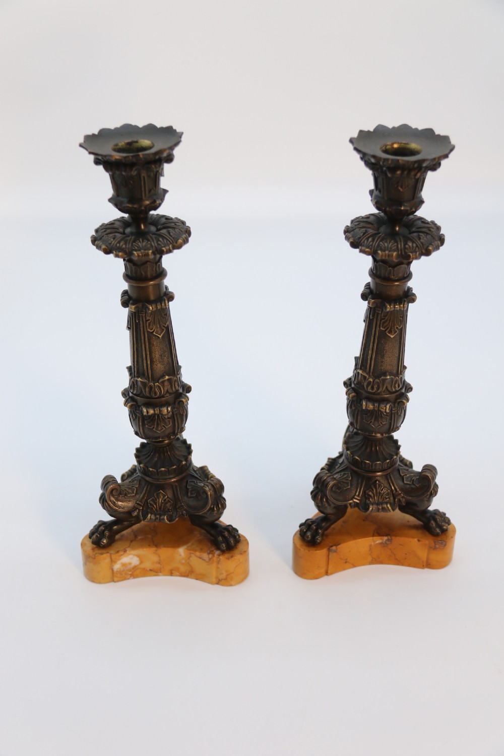A pair of antique French Empire dark bronze candlesticks with ornate floral carvings and claw feet, resting upon yellow sienna marble plinths. View VII