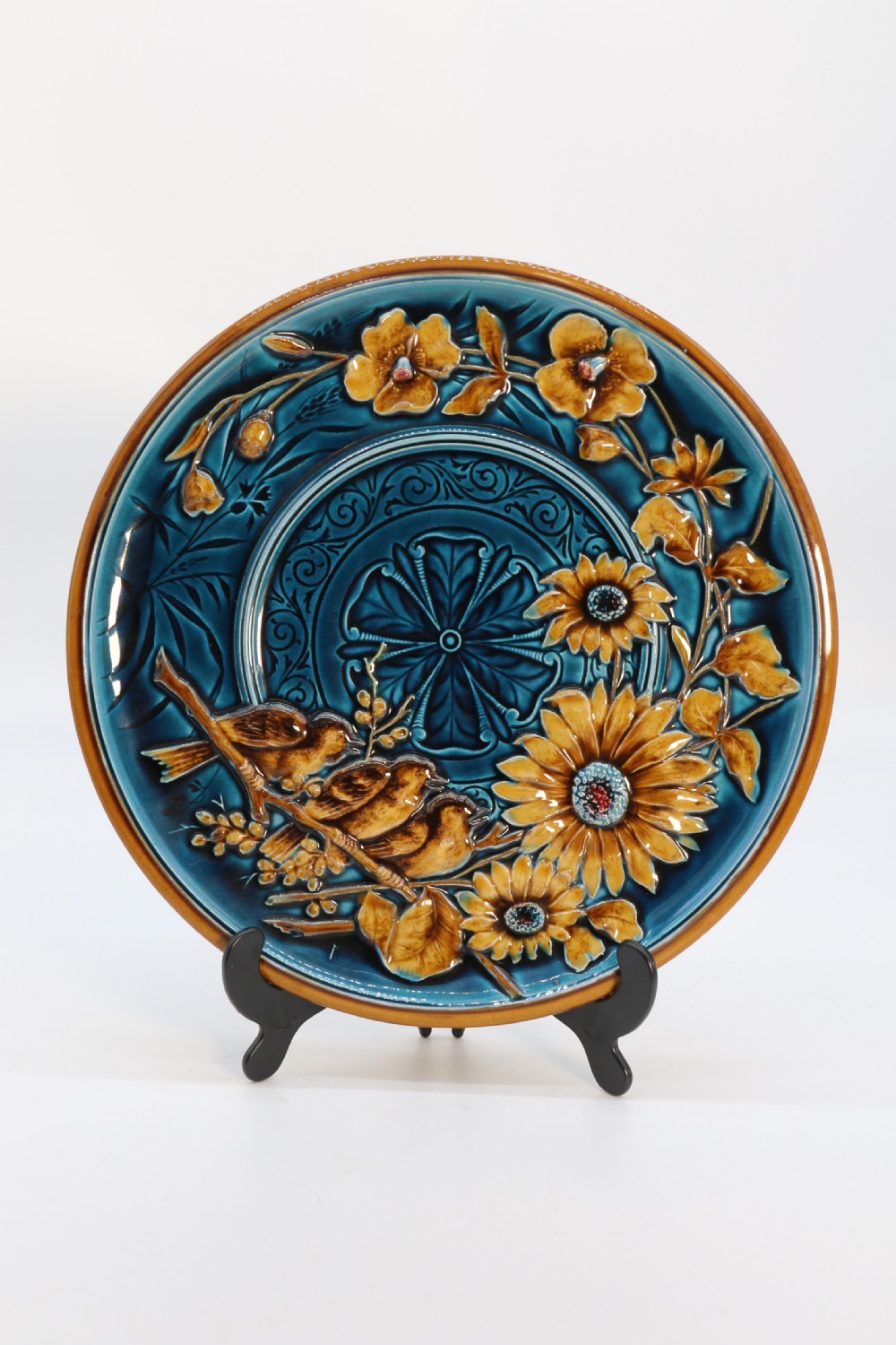 A circular late nineteenth-century Austrian majolica decorative plate featuring relief mouldings of birds perched on branches beside sunflowers over a teal glazed background.