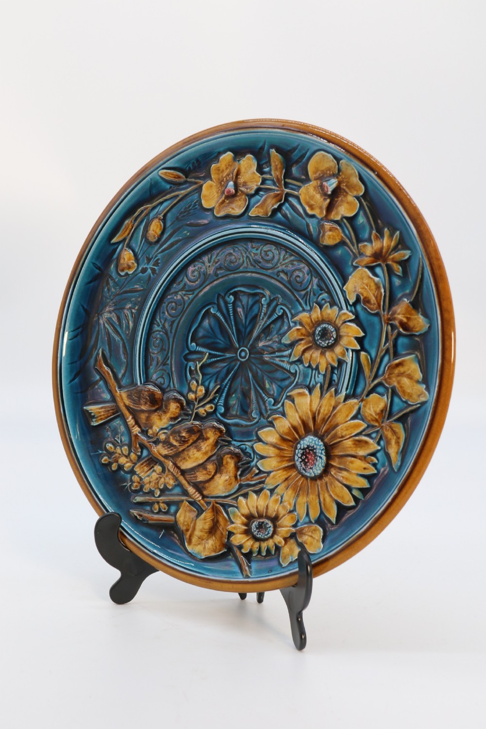 A circular late nineteenth-century Austrian majolica decorative plate featuring relief mouldings of birds perched on branches beside sunflowers over a teal glazed background. View V