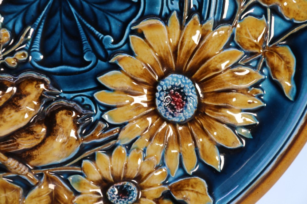 A circular late nineteenth-century Austrian majolica decorative plate featuring relief mouldings of birds perched on branches beside sunflowers over a teal glazed background. View XI