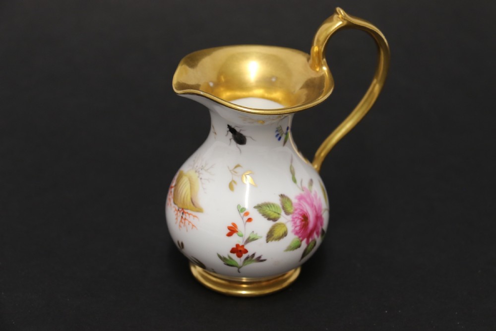A small white hard-paste porcelain ewer with a high looped gilded handle, flared gold interior rim, and hand-painted motifs including a butterfly, seashells, and botanical leaves. View III