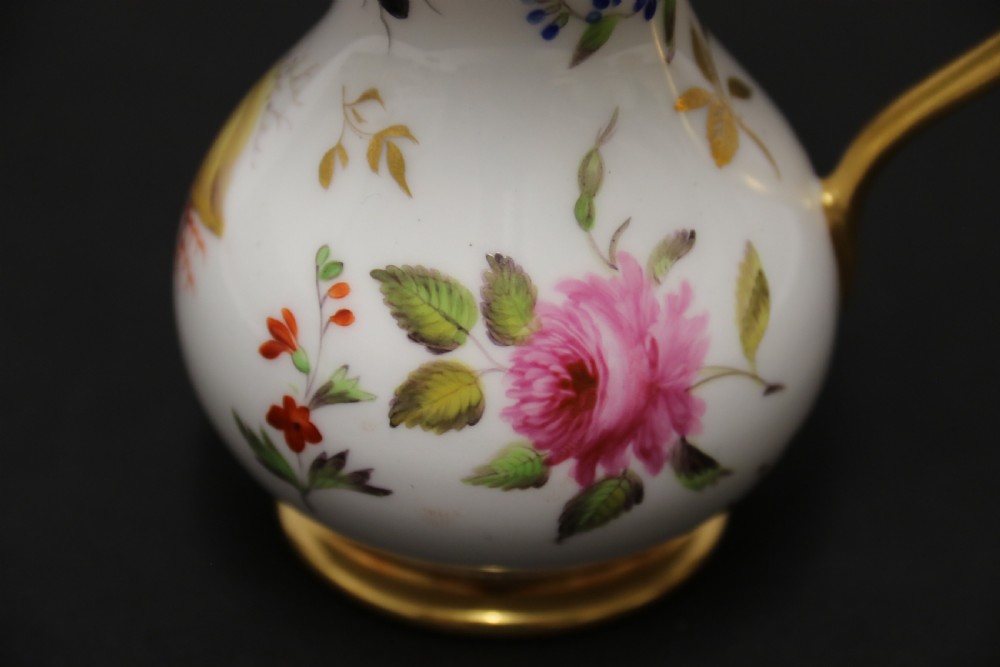 A small white hard-paste porcelain ewer with a high looped gilded handle, flared gold interior rim, and hand-painted motifs including a butterfly, seashells, and botanical leaves. View VIII