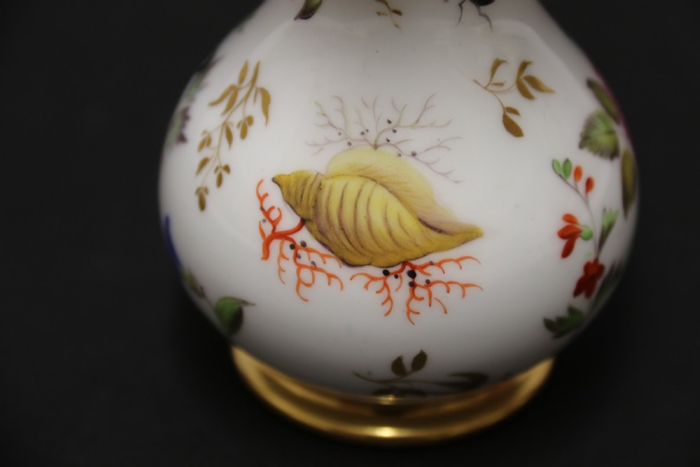 A small white hard-paste porcelain ewer with a high looped gilded handle, flared gold interior rim, and hand-painted motifs including a butterfly, seashells, and botanical leaves. View IX
