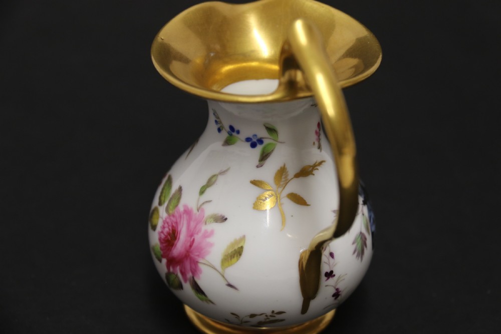 A small white hard-paste porcelain ewer with a high looped gilded handle, flared gold interior rim, and hand-painted motifs including a butterfly, seashells, and botanical leaves. View XIV