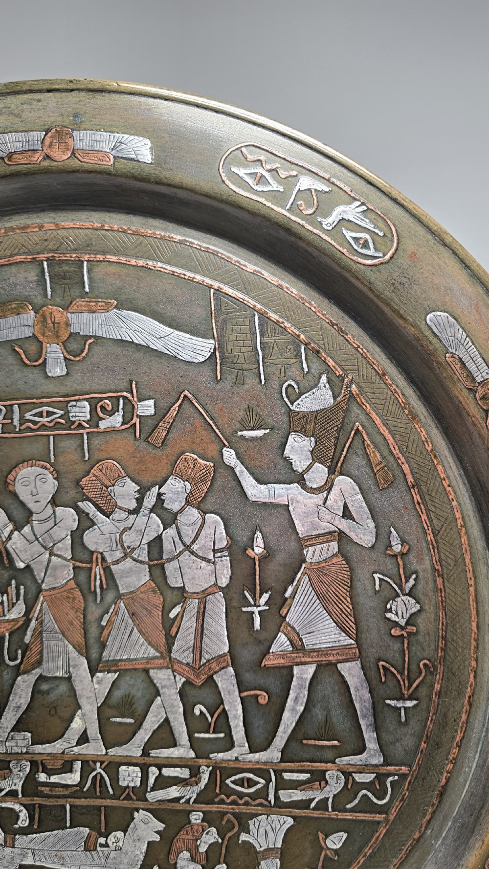 A circular bronze charger plate inlaid with silver and copper depicting ancient Egyptian figures, winged scarabs, and hieroglyphic motifs. View IV
