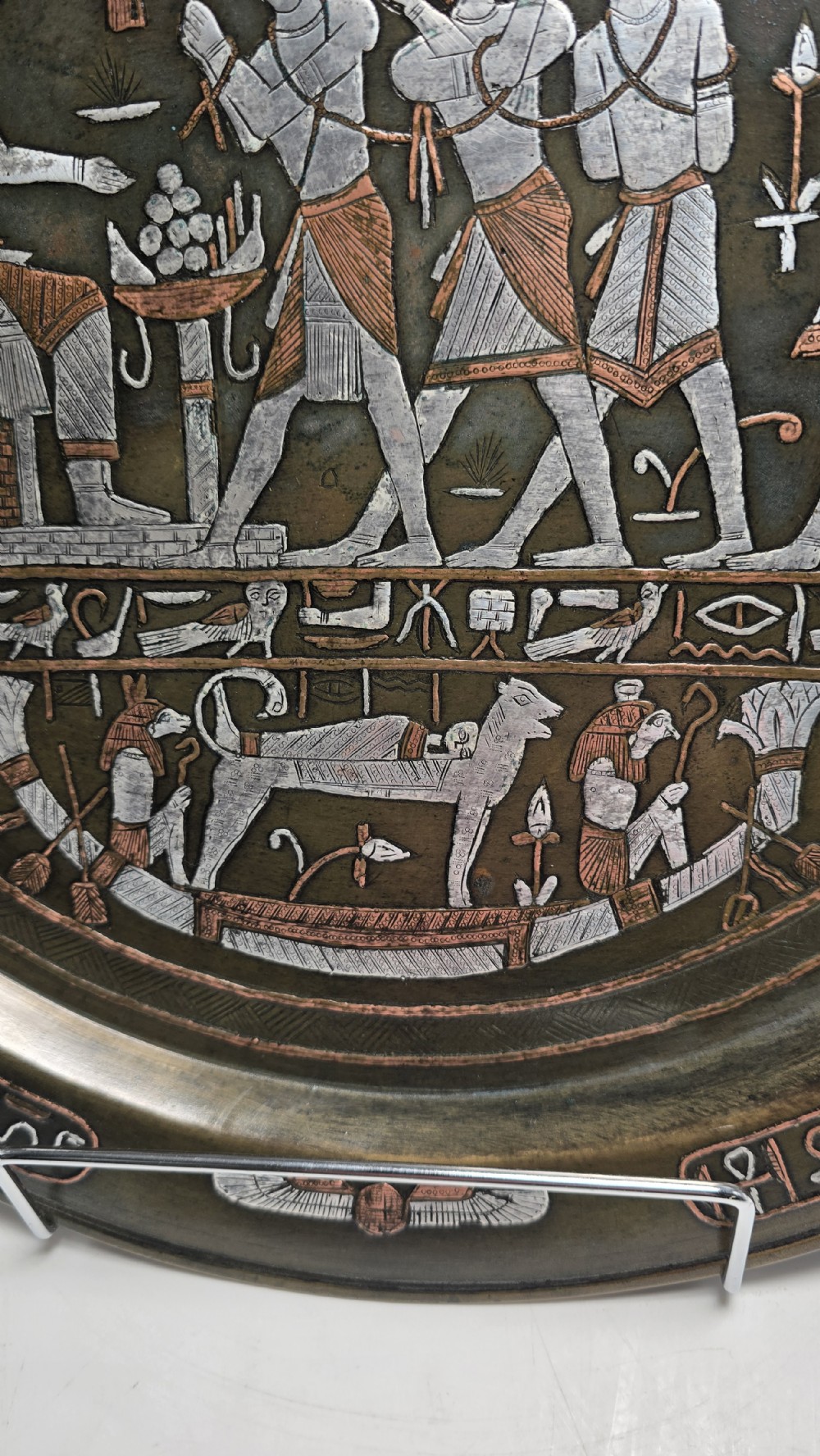 A circular bronze charger plate inlaid with silver and copper depicting ancient Egyptian figures, winged scarabs, and hieroglyphic motifs. View VI