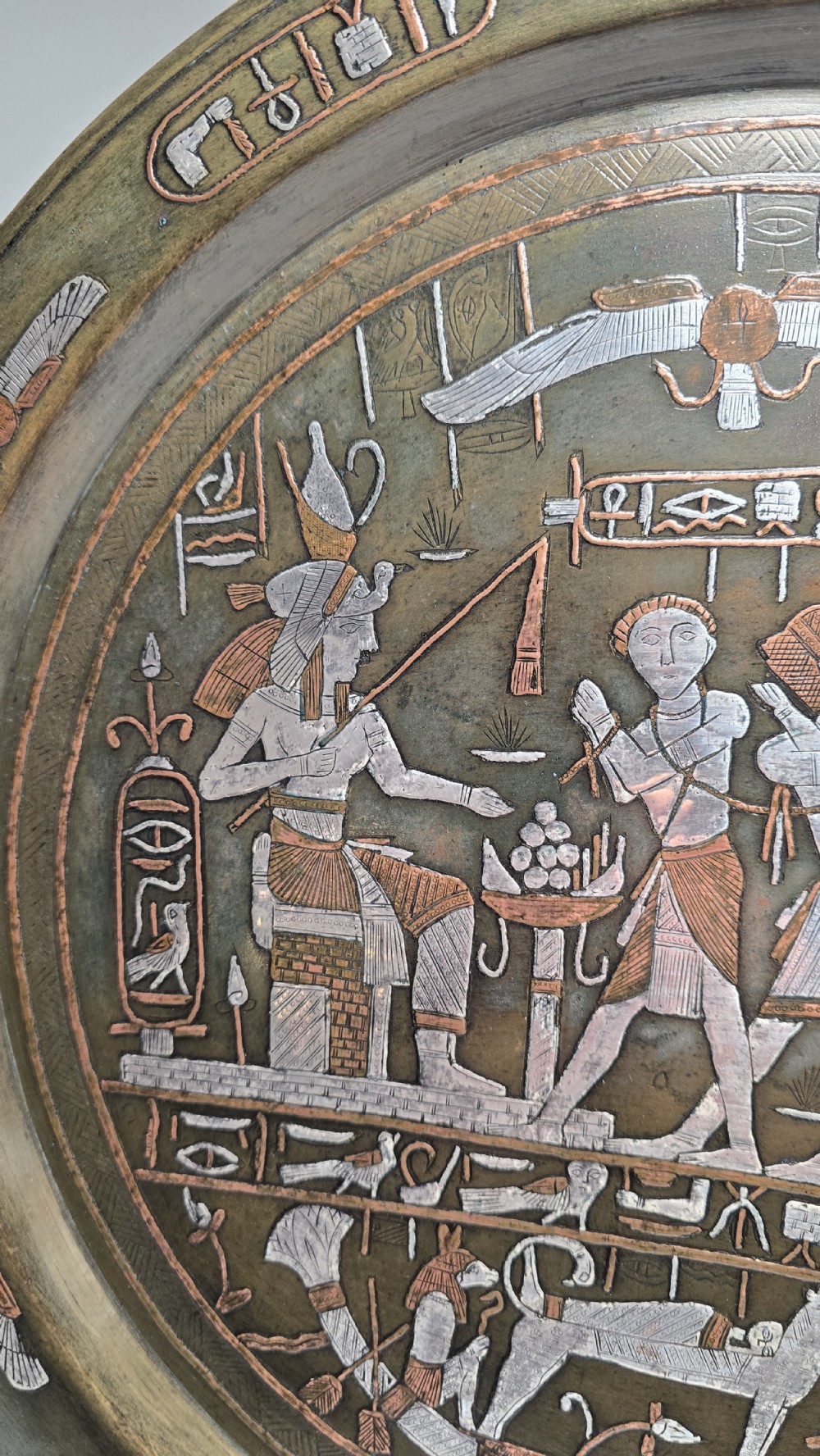 A circular bronze charger plate inlaid with silver and copper depicting ancient Egyptian figures, winged scarabs, and hieroglyphic motifs. View VIII