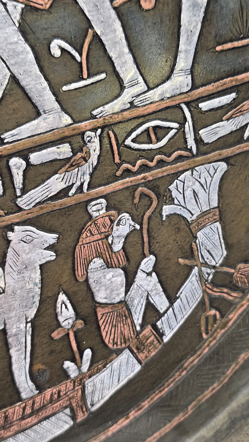 A circular bronze charger plate inlaid with silver and copper depicting ancient Egyptian figures, winged scarabs, and hieroglyphic motifs. View XVII