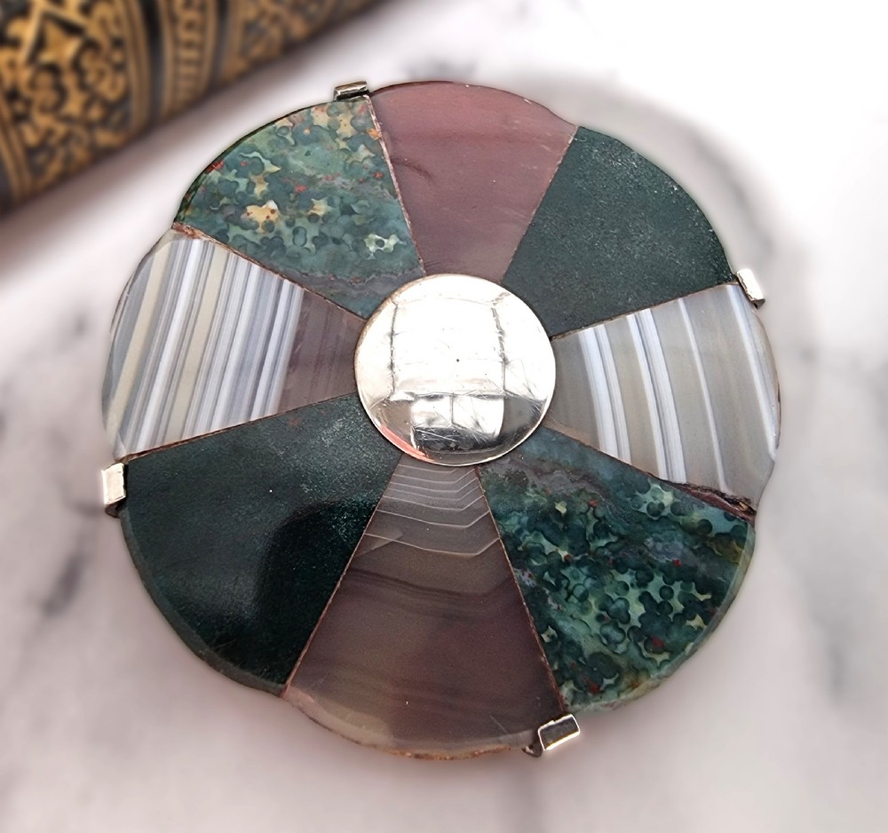 A late 19th-century circular Scottish silver brooch featuring segmented wedge inlays of varied banded agates and jaspers surrounding a central silver disc.