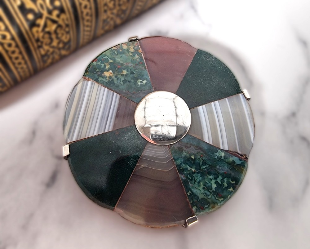 A late 19th-century circular Scottish silver brooch featuring segmented wedge inlays of varied banded agates and jaspers surrounding a central silver disc. View V