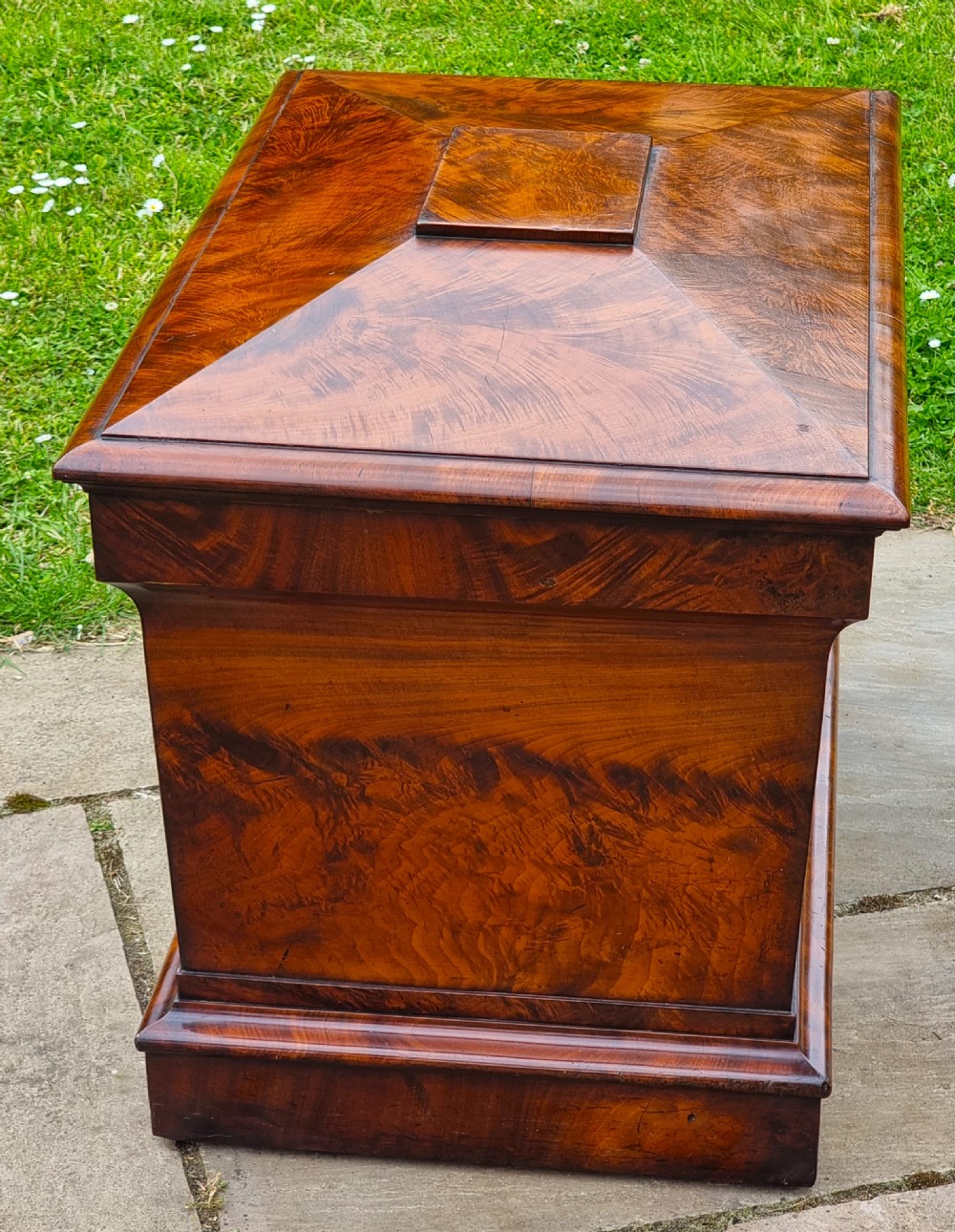 A Regency period sarcophagus-shaped wine cooler crafted from flame mahogany veneer with a stepped pediment lid and plinth base. View VII