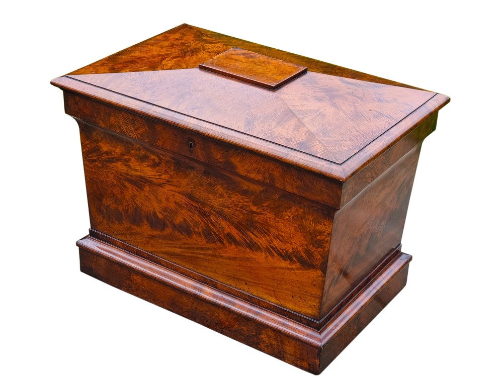 A Regency period sarcophagus-shaped wine cooler crafted from flame mahogany veneer with a stepped pediment lid and plinth base.