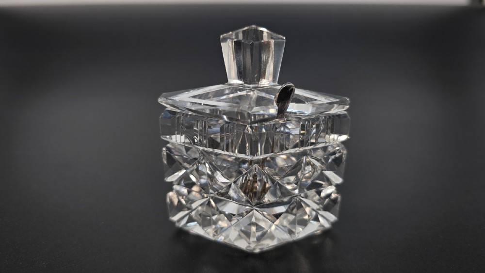 An Art Deco cut lead crystal five-piece cruet set featuring two stoppered bottles and two lidded pots arranged on an integral geometric glass tray. View VII