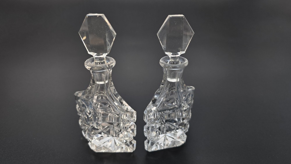 An Art Deco cut lead crystal five-piece cruet set featuring two stoppered bottles and two lidded pots arranged on an integral geometric glass tray. View IX