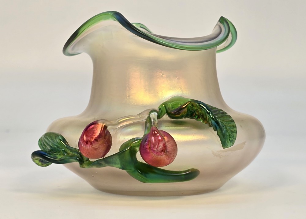 An Art Nouveau iridescent glass vase featuring a wavy green-rimmed mouth and hand-applied glass cherries with green leaves on the side.