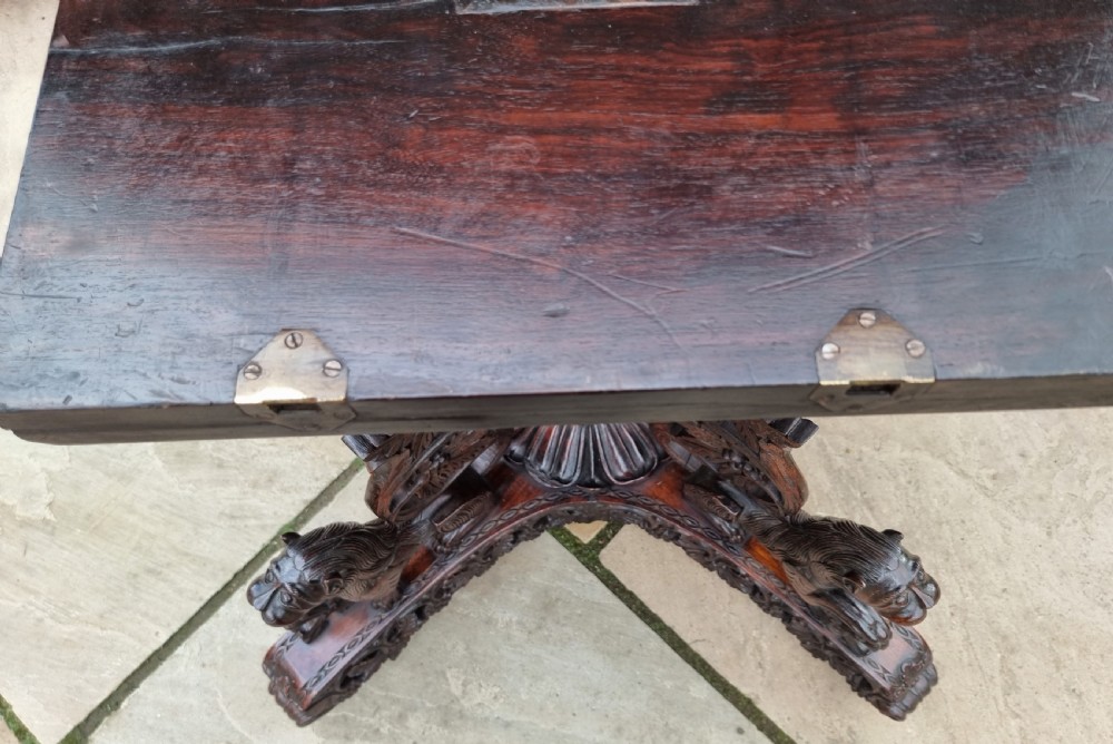 A 19th-century Anglo-Indian carved padauk wood centre table featuring a scalloped top, deeply carved pierced apron of foliage, and a pedestal base supported by carved mythical lion feet with brass castors. View XIII