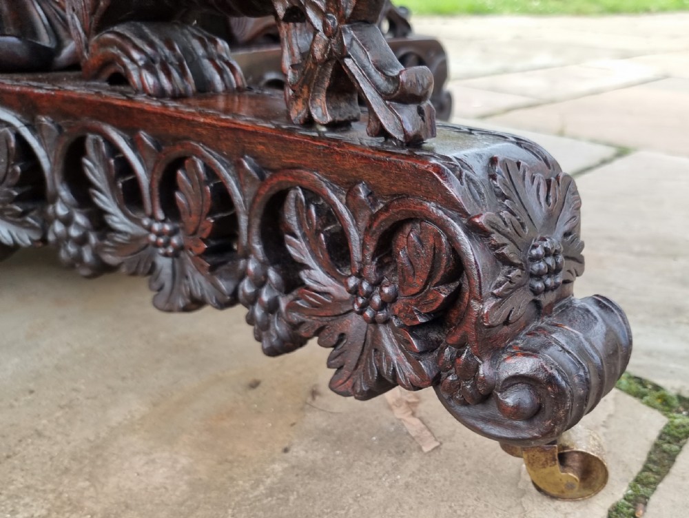 A 19th-century Anglo-Indian carved padauk wood centre table featuring a scalloped top, deeply carved pierced apron of foliage, and a pedestal base supported by carved mythical lion feet with brass castors. View XXI