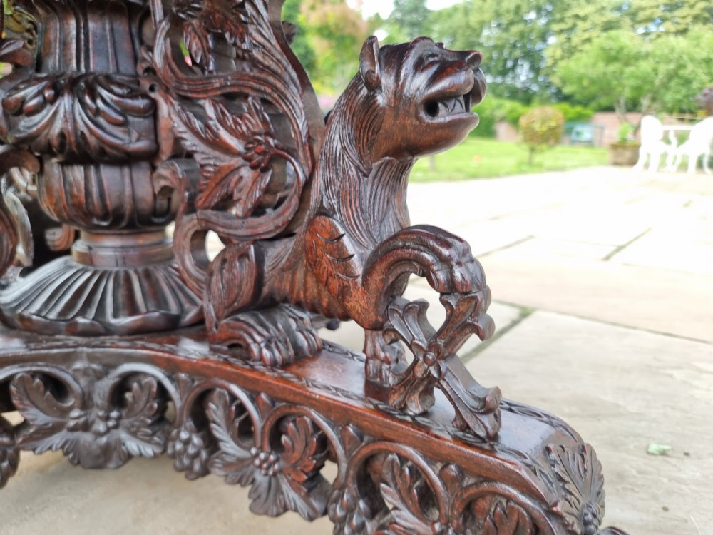 A 19th-century Anglo-Indian carved padauk wood centre table featuring a scalloped top, deeply carved pierced apron of foliage, and a pedestal base supported by carved mythical lion feet with brass castors. View XXII