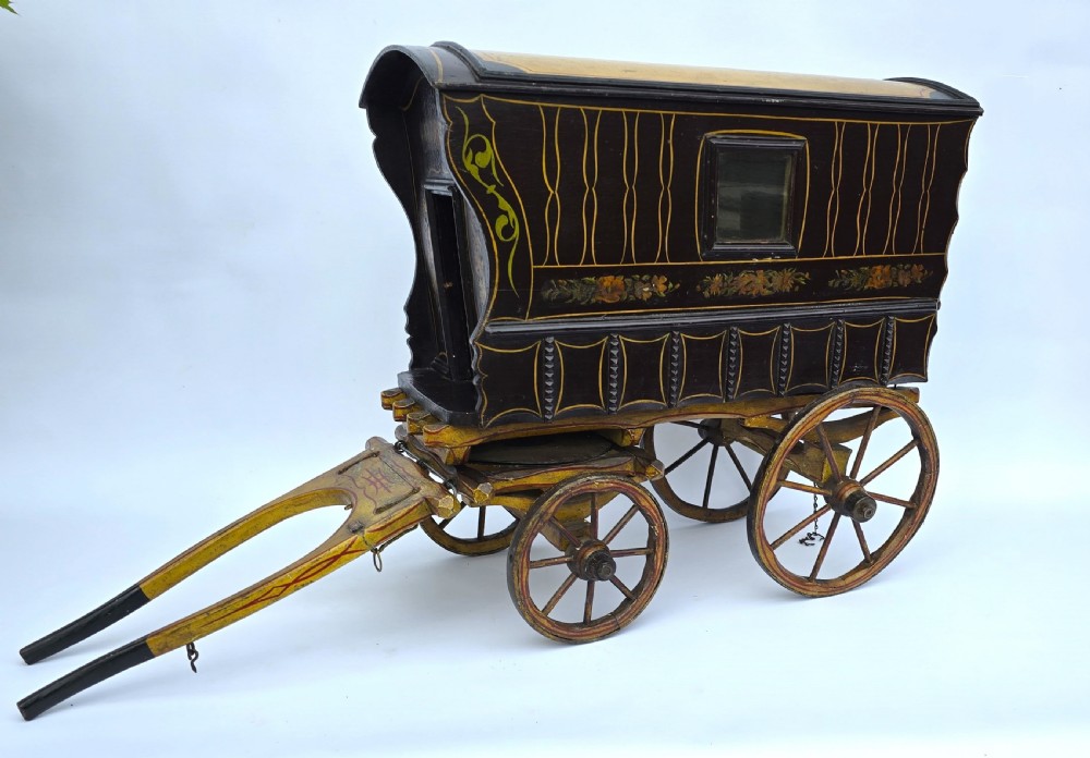 An antique hand-painted wooden model of a Romani gypsy caravan vardo with yellow spoked wheels and floral detail. View II