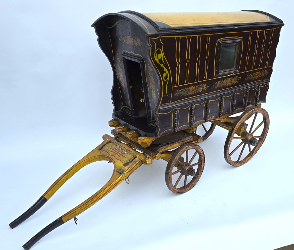 An antique hand-painted wooden model of a Romani gypsy caravan vardo with yellow spoked wheels and floral detail. View III