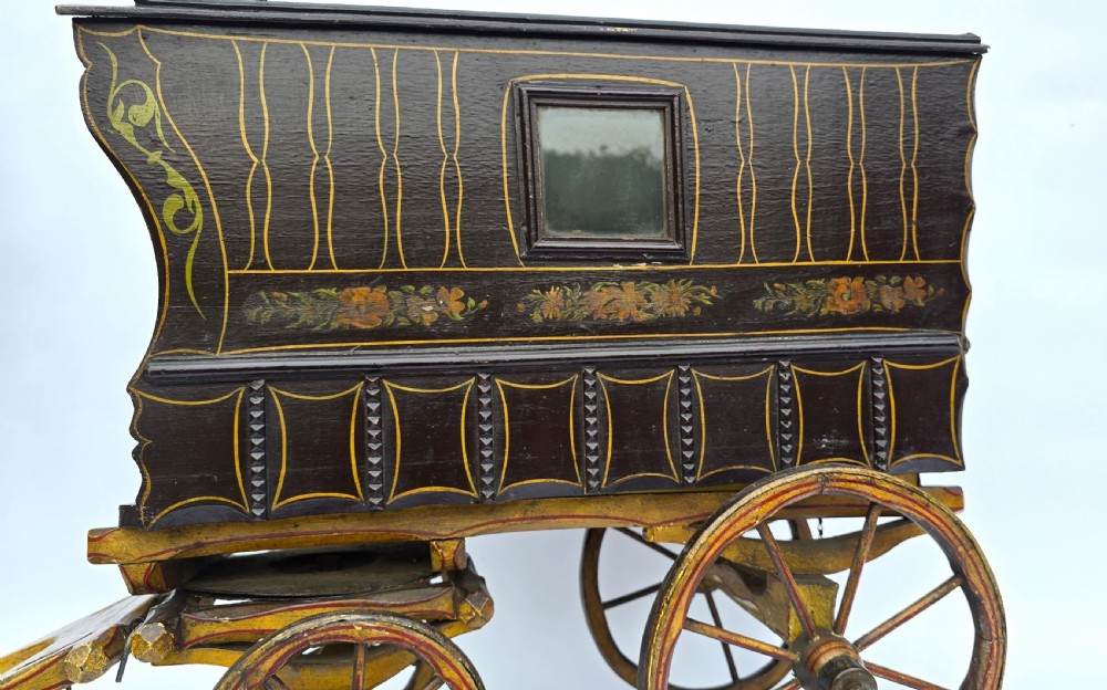 An antique hand-painted wooden model of a Romani gypsy caravan vardo with yellow spoked wheels and floral detail. View X