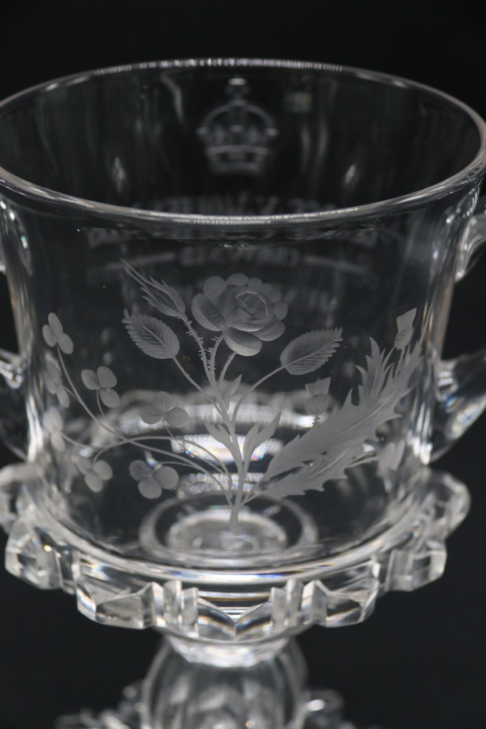 A clear glass commemorative goblet with two loop handles, wheel-engraved with text for the 1911 coronation of King George V and Queen Mary, supported by a faceted stem and starburst base. View V