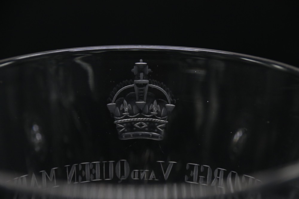 A clear glass commemorative goblet with two loop handles, wheel-engraved with text for the 1911 coronation of King George V and Queen Mary, supported by a faceted stem and starburst base. View VI