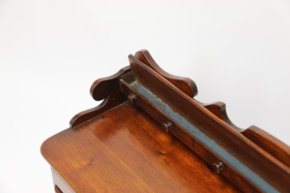 A nineteenth-century miniature mahogany dresser base featuring a shaped gallery back with pegs, multiple small drawers with turned knobs, and a central panelled cupboard door resting on turned feet. View XIV