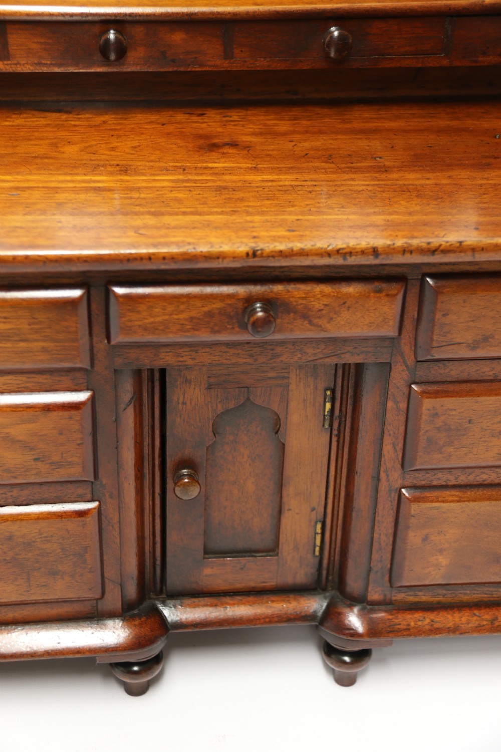 A nineteenth-century miniature mahogany dresser base featuring a shaped gallery back with pegs, multiple small drawers with turned knobs, and a central panelled cupboard door resting on turned feet. View XIX