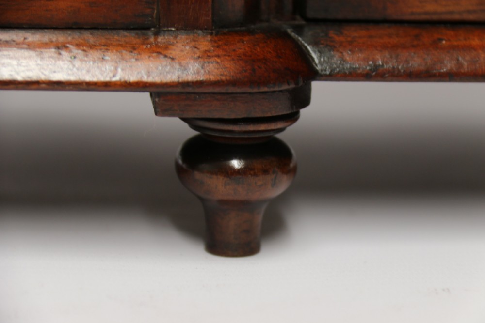 A nineteenth-century miniature mahogany dresser base featuring a shaped gallery back with pegs, multiple small drawers with turned knobs, and a central panelled cupboard door resting on turned feet. View XXI