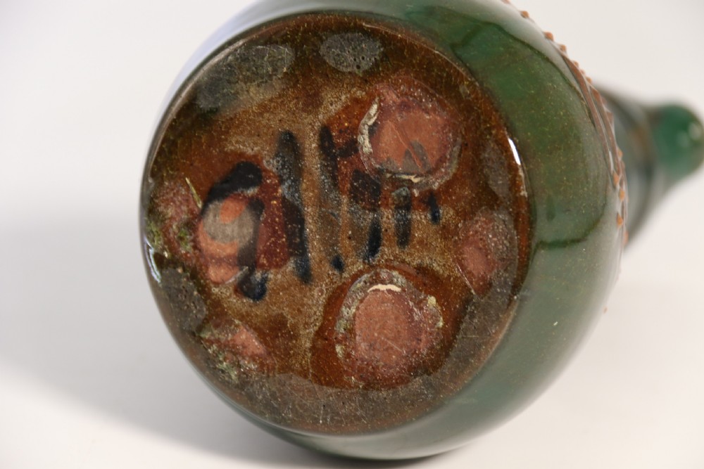 A green glazed ceramic jug featuring a flared spout, loop handle, and an embossed sunflower motif on the side. View IX