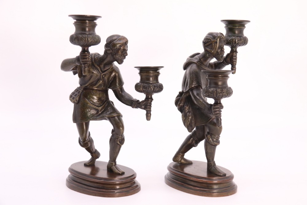 A pair of 19th-century patinated dark bronze double candlesticks featuring sculpted male figures standing on oval bases and holding two sconces each. View X