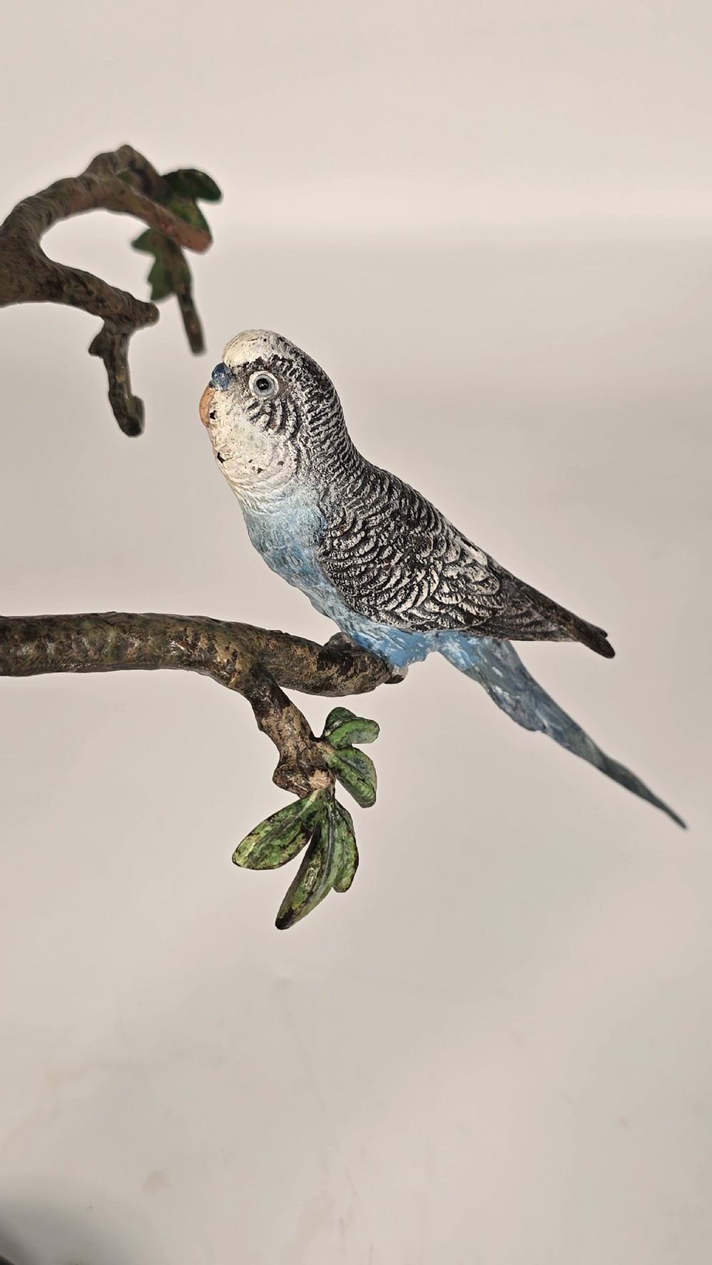 A cold painted bronze sculpture depicting three blue budgerigars perched on a branch mounted on an oval dark marble base. View XII
