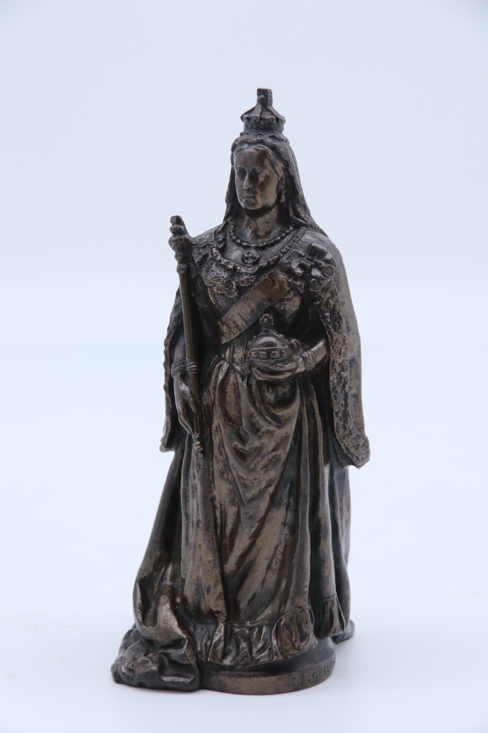 A dark patinated bronze statuette depicting Queen Victoria standing in full ceremonial robes, wearing a crown and holding a sceptre and orb.