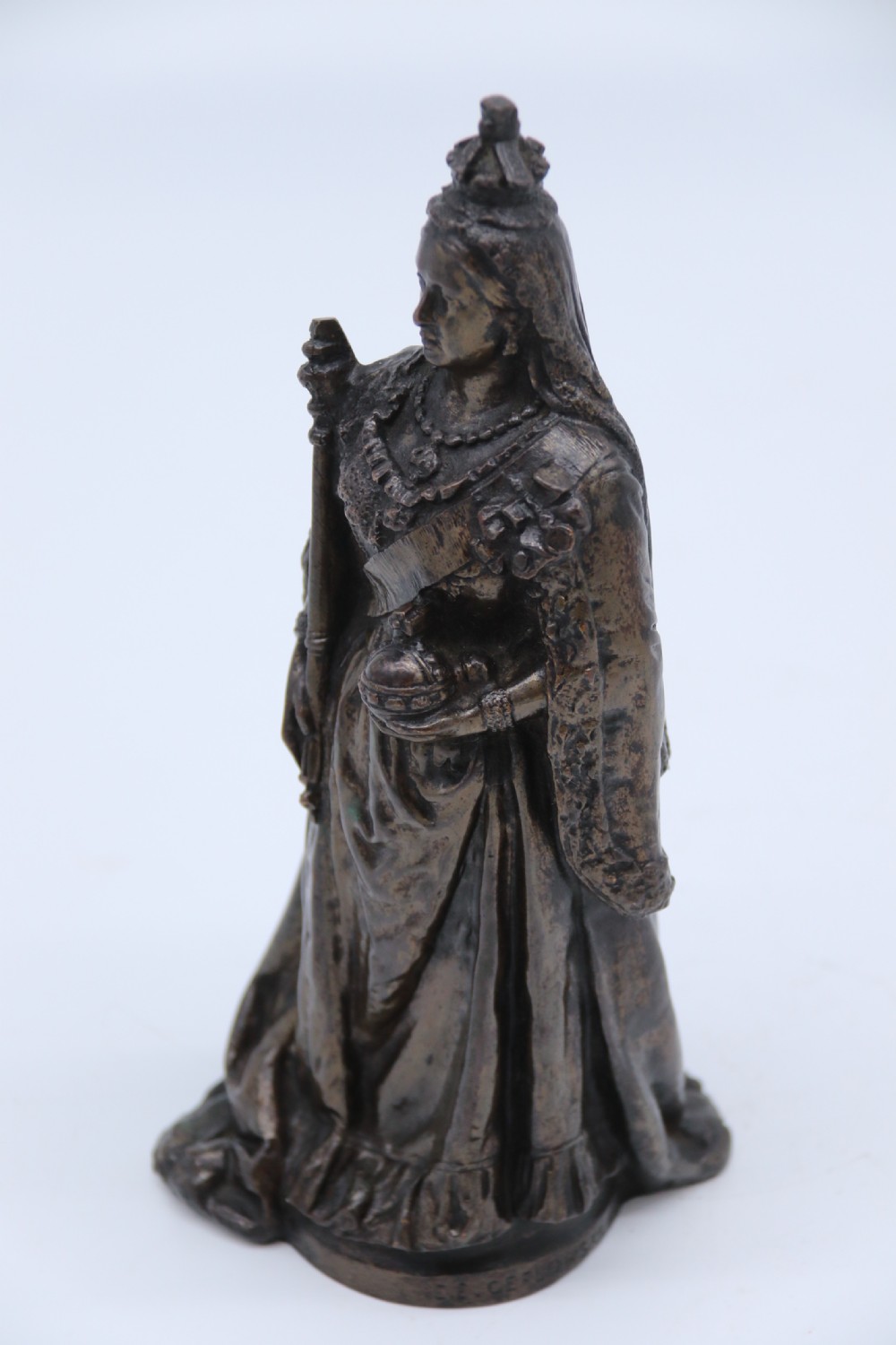 A dark patinated bronze statuette depicting Queen Victoria standing in full ceremonial robes, wearing a crown and holding a sceptre and orb. View III