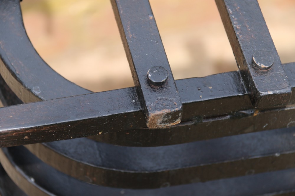 A black wrought iron fire basket featuring a curved slatted log cradle, scrolled corner terminals, and riveted front bars. View II