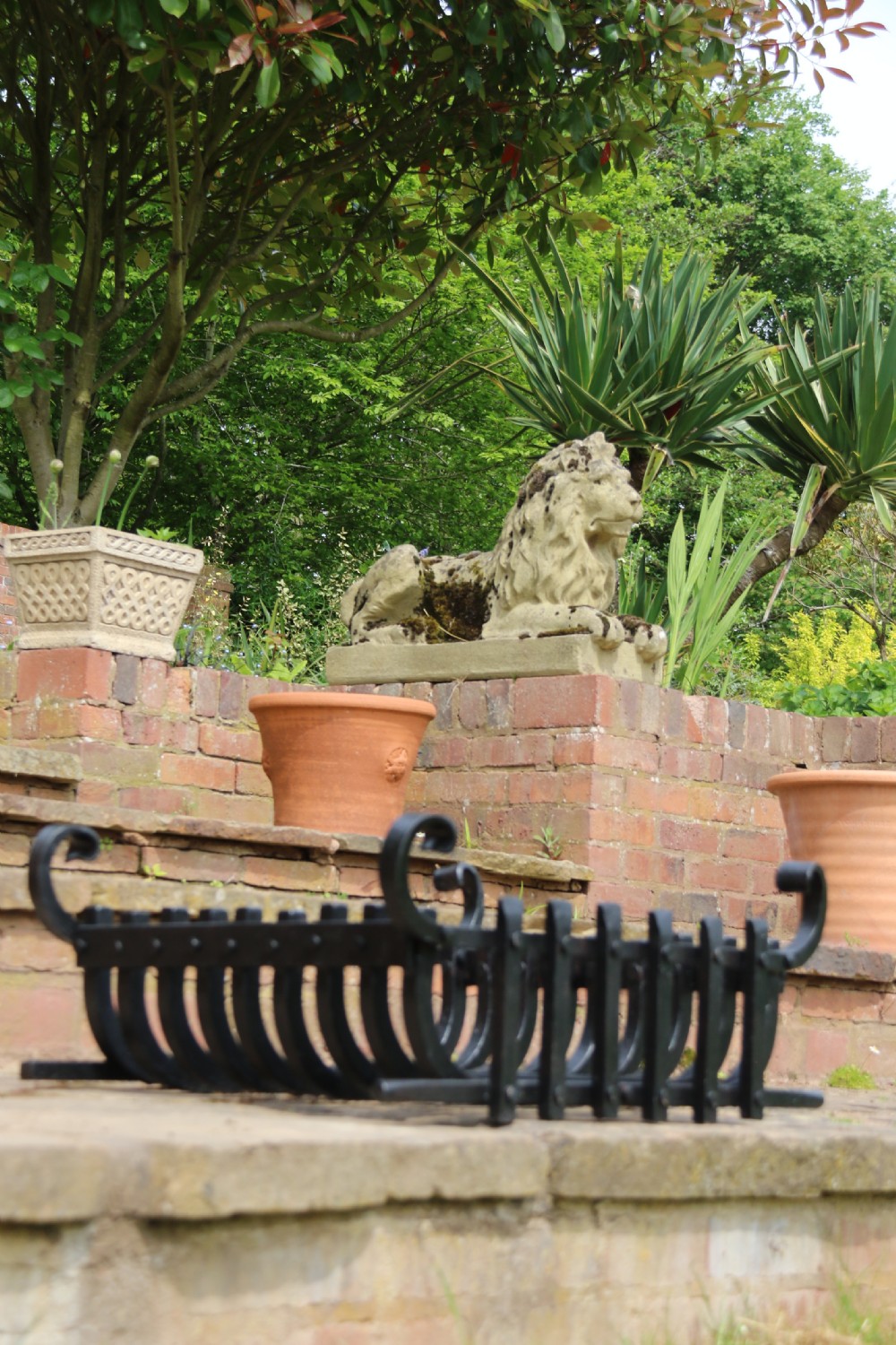A black wrought iron fire basket featuring a curved slatted log cradle, scrolled corner terminals, and riveted front bars. View V