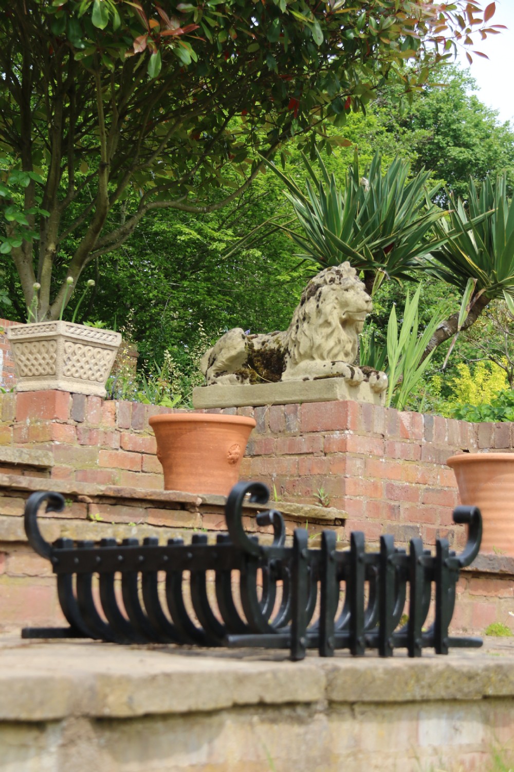 A black wrought iron fire basket featuring a curved slatted log cradle, scrolled corner terminals, and riveted front bars. View VI