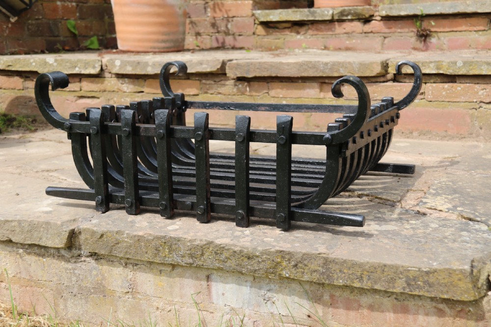 A black wrought iron fire basket featuring a curved slatted log cradle, scrolled corner terminals, and riveted front bars. View VIII