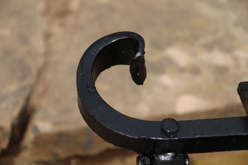 A black wrought iron fire basket featuring a curved slatted log cradle, scrolled corner terminals, and riveted front bars. View XII