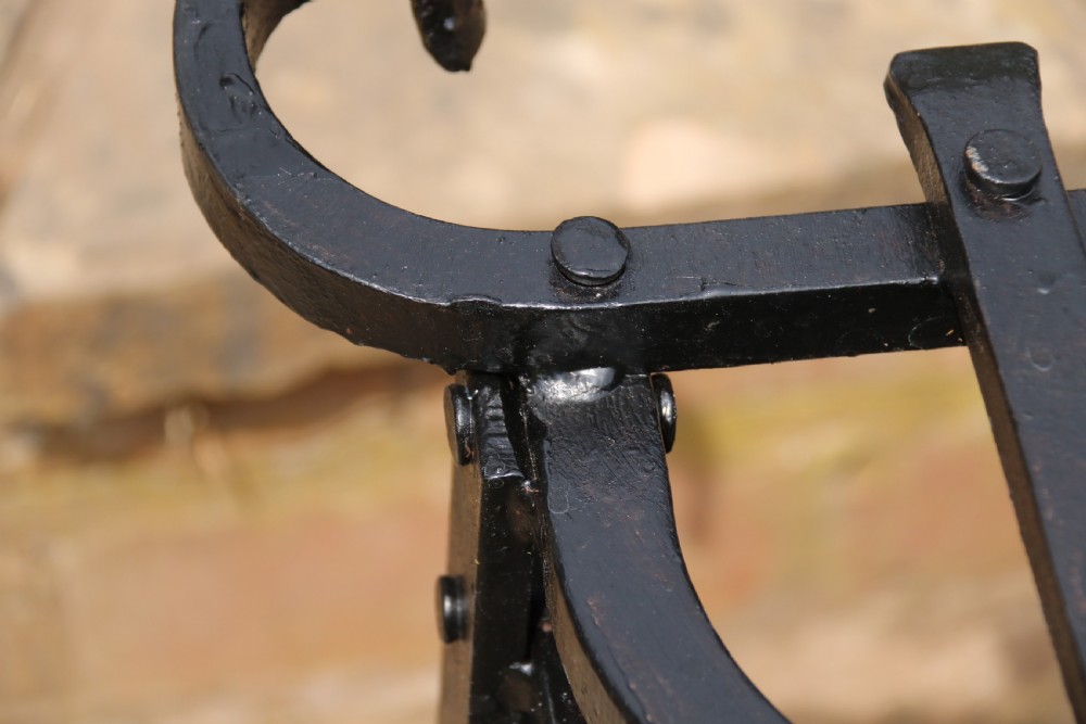 A black wrought iron fire basket featuring a curved slatted log cradle, scrolled corner terminals, and riveted front bars. View XIII