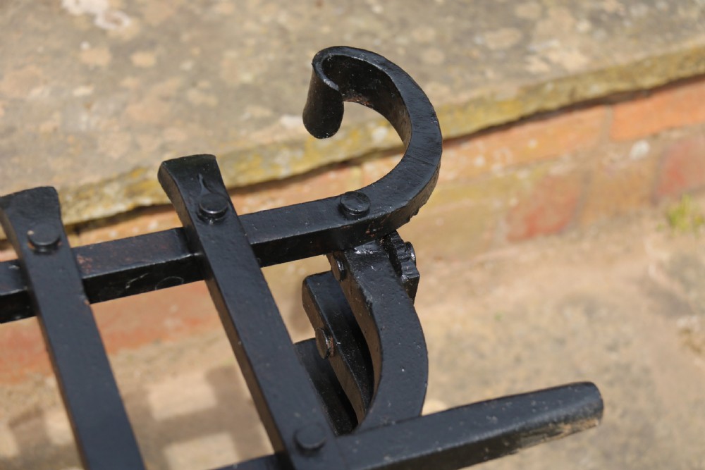 A black wrought iron fire basket featuring a curved slatted log cradle, scrolled corner terminals, and riveted front bars. View XIV