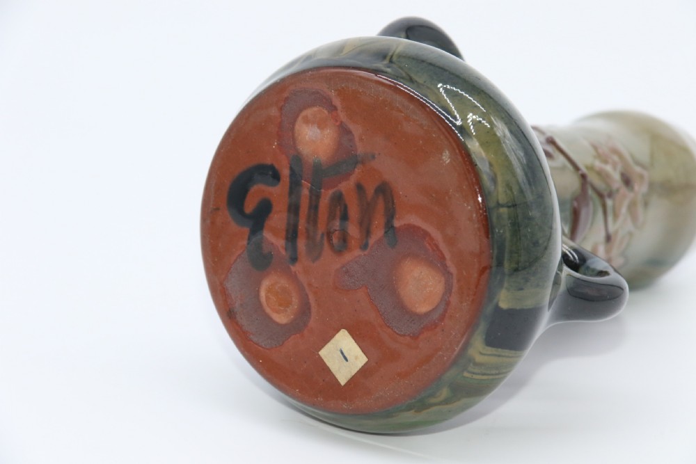 A green and brown glazed earthenware ceramic vase featuring three handles and raised slipware floral decoration. View VI