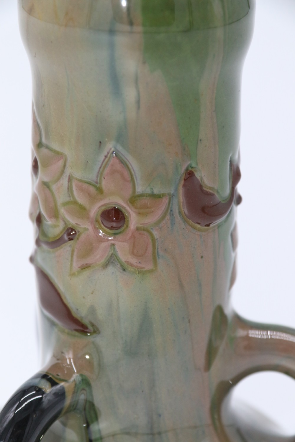 A green and brown glazed earthenware ceramic vase featuring three handles and raised slipware floral decoration. View IX